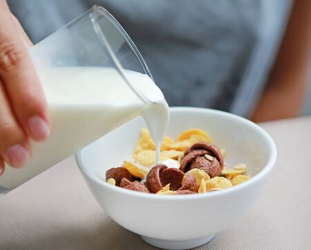 Milk pouring into bowl of muesli on table