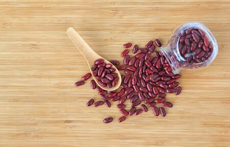 Red soybeans on bamboo wooden board with glass bottle and wooden spoon, top view