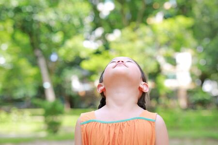 little Asian child girl close their eyes in garden with Breathe fresh air from nature. Portrait of kid relax in green park for good health.の写真素材