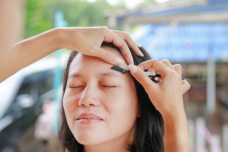 Asian woman with makeup artist used eyebrow razor makeup for pretty face close up.