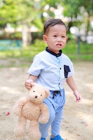 Funny face Asian little boy walking with teddy bear at garden outdoor.の写真素材