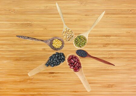 Variety of Whole grain beans in wood spoon against bamboo wood board texture