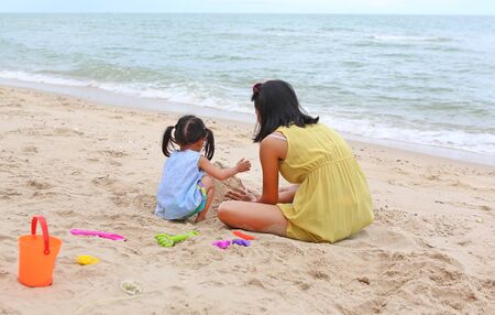 Happy loving family. Mother and her daughter child girl playing sand with animal block forming at the beachの写真素材