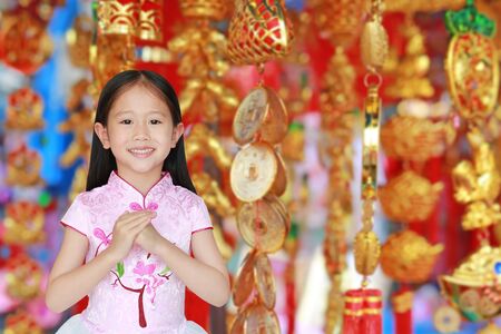 Happy little Asian girl wearing pink Traditional Chinese dress wishing you a happy Chinese New Year on luck item background.の写真素材