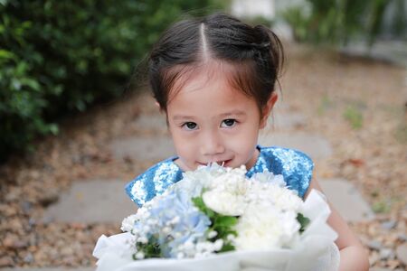 Adorable little Asian child girl with Bouquet of flowers in the garden.の写真素材