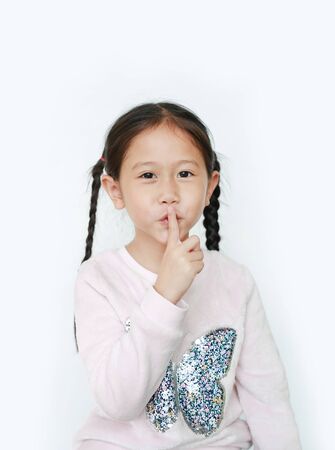 Little child girl with finger up to lips for making a quiet gesture isolated on white background. Kid showing shh sign.の写真素材