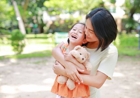 Portrait of happy Asian mother cuddle daughter and hugging teddy bear doll in the garden. Mom and child girl with love and relationship concept.の写真素材