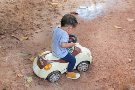 Little Asian boy driving toy car outdoors.の写真素材