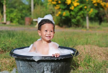 Happy asian baby boy take a bath with foam bubble and washing in black plastic basin in nature outdoor.の写真素材