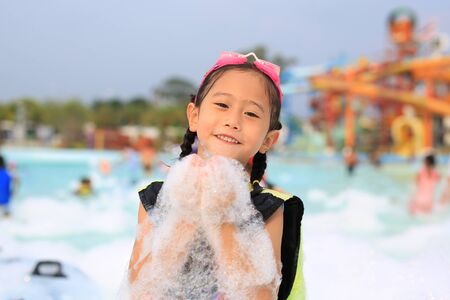 Happy little Asian child girl smiling having fun in Foam Party at the pool outdoor.の写真素材