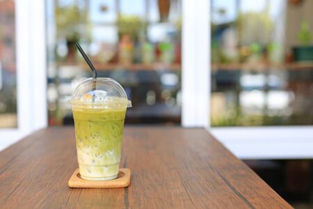Iced matcha green tea latte with milk with brown straw in take away cup on wooden table at cafe.の写真素材