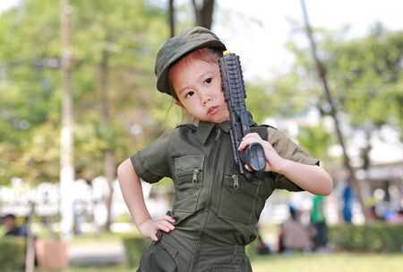 Little Asian child girl in pilot soldier suit costume with holding gun in hands at the garden.の写真素材