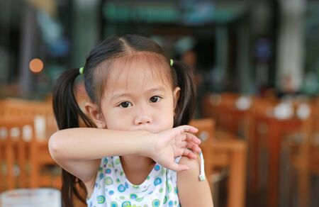Cute little Asian child girl wiping her mouth by her arm after meal with looking camera.の写真素材