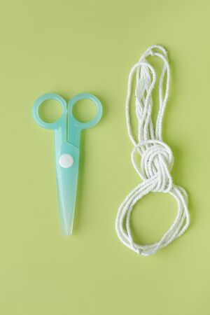 Cyan Plastic children safety scissors with rope on green background.
