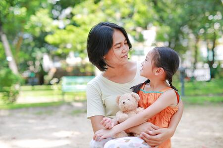 Portrait of happy Asian mother cuddle daughter and hugging teddy bear doll in the garden. Mom and child girl with love and relationship concept.の写真素材