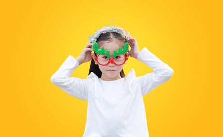 Adorable little Asian girl reindeer putting on the head of multi-color paper spray on yellow background. A moment of celebration concept.の写真素材