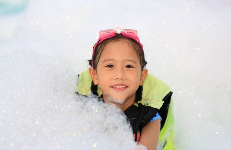 Portraits of happy little Asian child girl smiling having fun in Foam Party at the pool outdoor.の写真素材