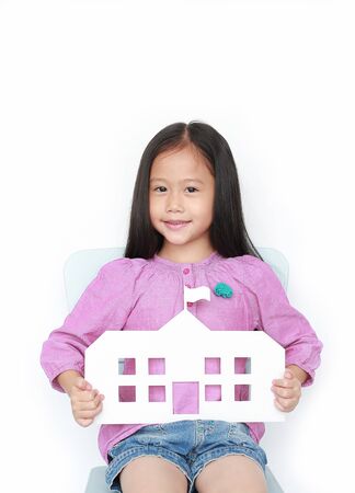 Smiling little Asian child girl holding mock-up paper school sitting on kid chair isolated over white background. Education and back to school concept.の写真素材