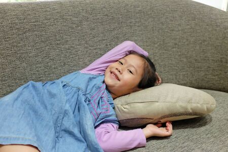 Adorable little Asian girl lying on grey sofa.