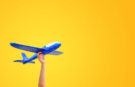 Close-up kid hand raise up a blue toy airplane flying isolated over yellow background with copy space.の写真素材