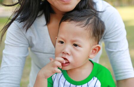 Close up Asian little baby boy eating by finger some orange fruit sitting with mother in the garden.の写真素材