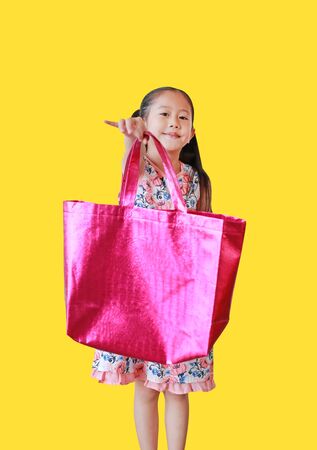 Little Asian girl showing a vibrant pink bag isolated on yellow background. Reuse for reduce global warming concept. Focus at kid face.の写真素材