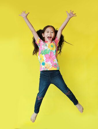 Happy asian little child girl wearing a floral pattern summer dress jumping and freedom movement on air isolated on yellow background. Holiday and summer fashion concept.の写真素材