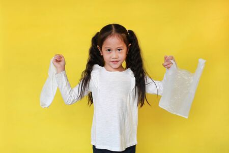 Cute asian little child girl holding a white thin polythene plastic bag isolated on yellow...