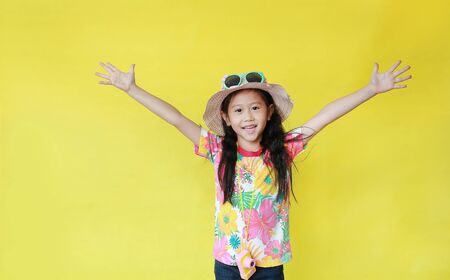 Smiling asian little child girl wearing a floral pattern summer dress and hat with sunglasses isolated on yellow background. Holiday and summer fashion concept.の写真素材
