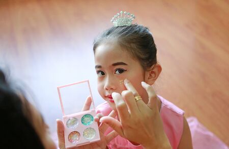 Closeup little Asian ballerina girl with glister makeup by her mother.