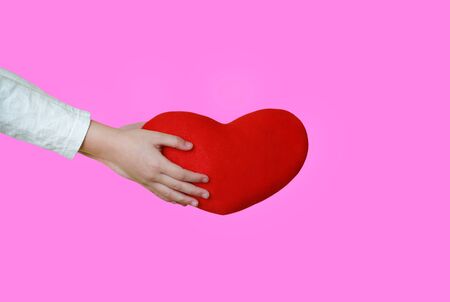 Close up children hands holding a red heart for you isolated on pink background. Love and valentine concept.の写真素材