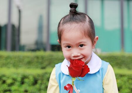 Close-up Asian child girl kissing red rose flower in the garden.の写真素材