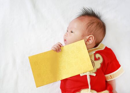 Infant baby boy in cheongsam with holding gold envelope lying on white fur background.の写真素材