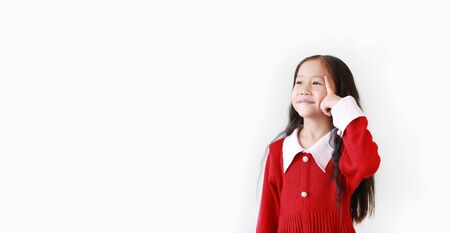 Pretty Asian little child girl in Scarlet red dress thinking expression and pointing index finger to head. Kid looking up for great idea or good memory isolated over white background with copy space.の写真素材