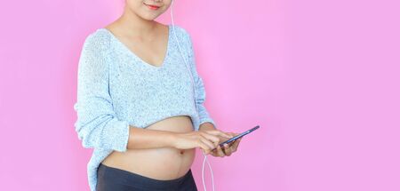 Closeup happy young asian pregnant woman with using smartphone isolated on pink background with copy space.の写真素材