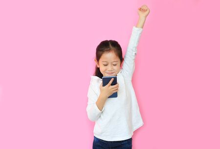 Surprised happy asian little child girl watching her smartphone and expression hand fight sign over...