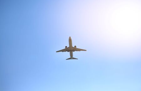 Airplane flying on blue sky background with rays of sunlight. Below view