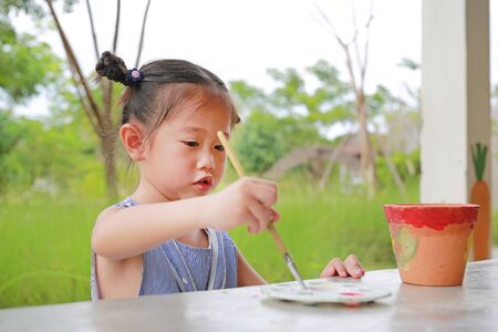 Asian kid girl paint on earthenware dish.