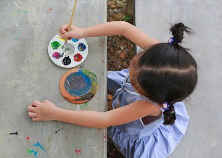Asian little kid girl painting on earthenware dish. View on top.の写真素材