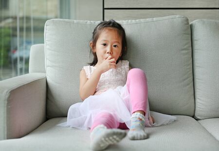 Little girl eating sausage on the sofa