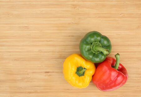 Green, red and yellow bell pepper on wooden board background