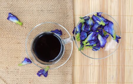 Butterfly pea or blue pea flower juice and flowers on sack and wooden mat background.の写真素材