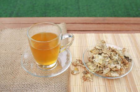 Chrysanthemum juice in glass cup and dried Chrysanthemum flower on wood background against green grass backgroundの写真素材