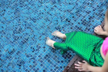 Cute little Asian child girl in a mermaid suit has fun sitting poolside.の写真素材