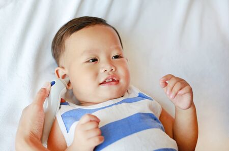 Mother takes temperature for baby boy with ear thermometer on bed at home.の写真素材