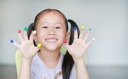 Adorable little Asian girl with colorful fingers painted in the children room.
