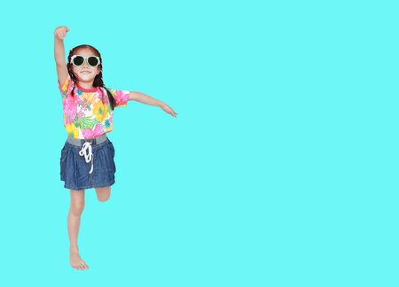 Happy little Asian kid girl wearing a flowers summer dress and sunglasses isolated on cyan background with copy space. Summer fashion kid concept.の写真素材