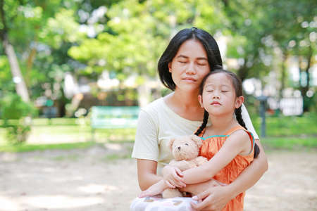 Portrait of Asian mother cuddle daughter and hugging teddy bear doll in the garden. Mom and child girl with love and relationship concept.の写真素材