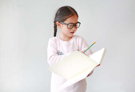 Asian Schoolgirl wearing eyeglasses holding and writes in a notebook with pencil on white background.の写真素材