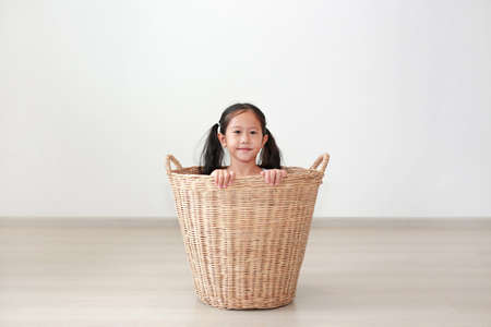 Portrait asian little child girl sitting in rattan basket in room at homeの写真素材